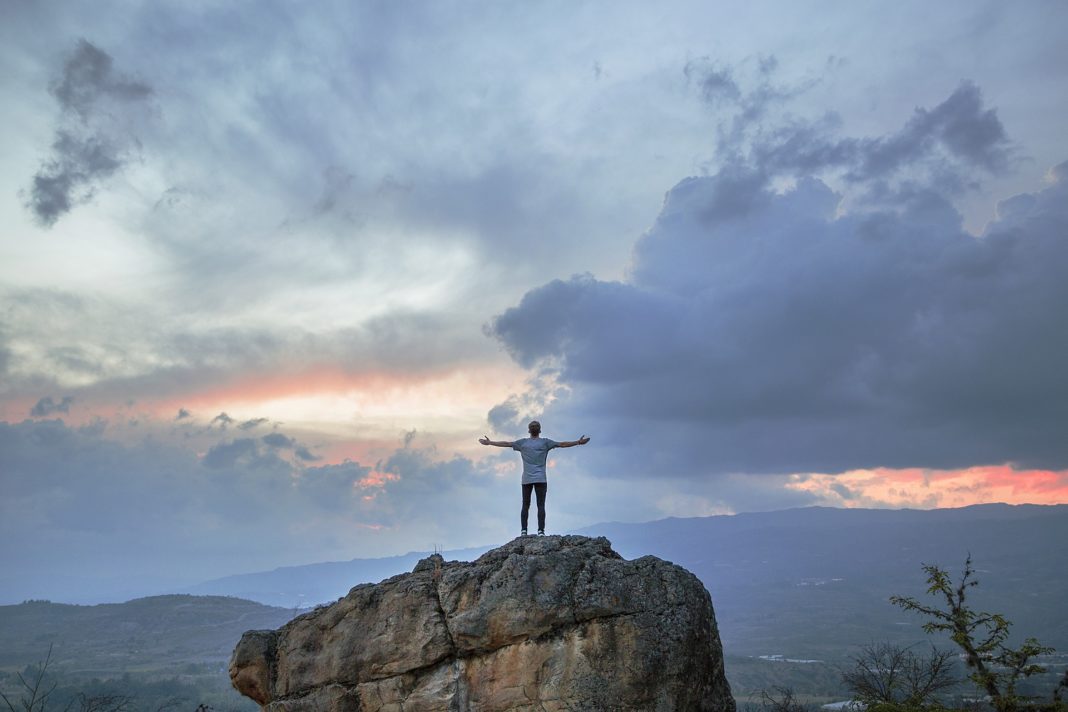 A man posing on a mountain top as the sun sets